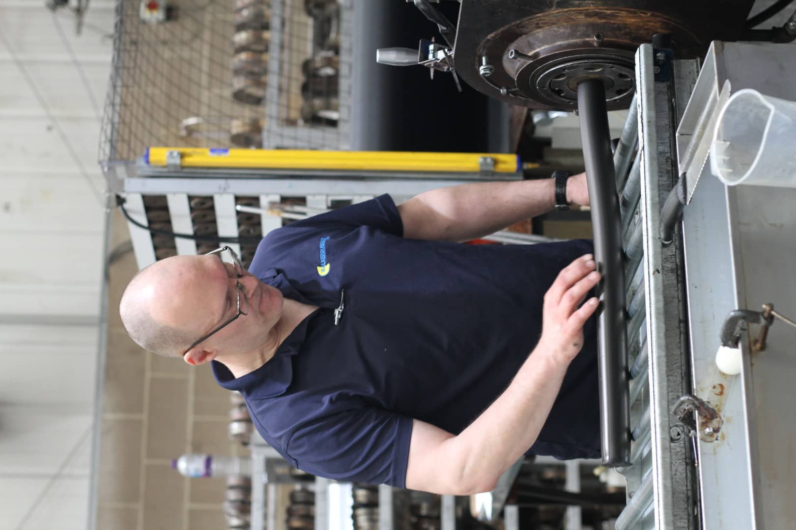 Manufacturing technician stands in busy factory setting while guiding rubber extrusion onto metal roller rack