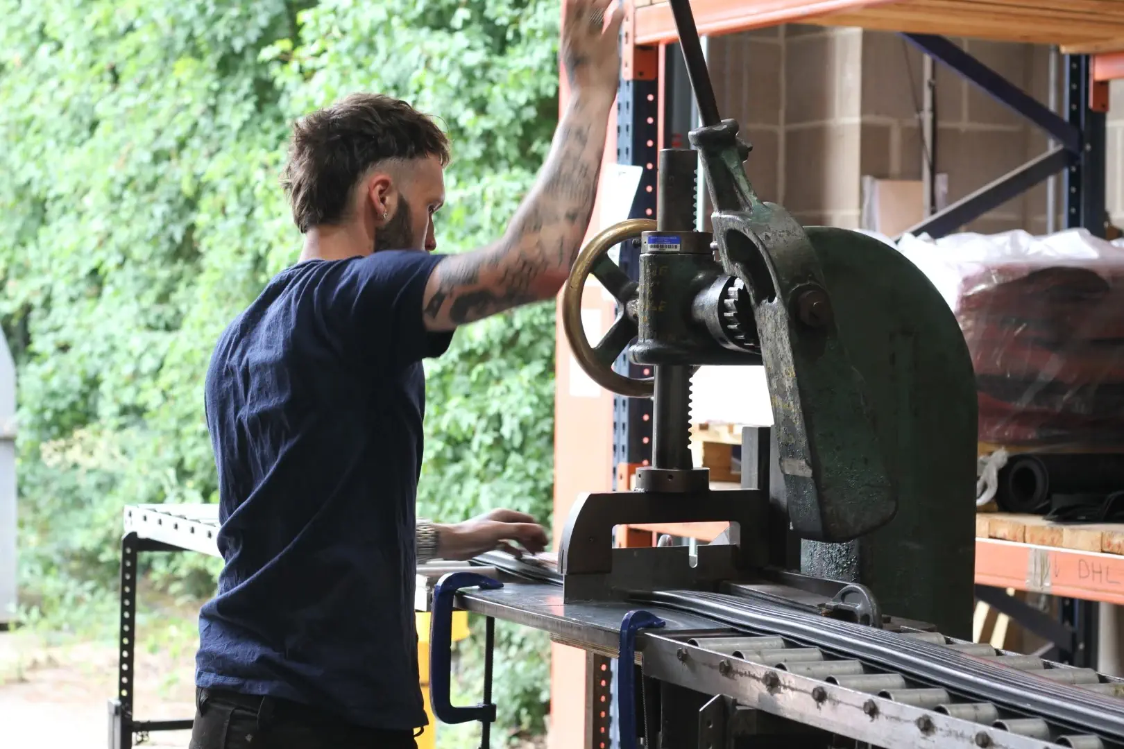 A manufacturing technician pulls the lever on a large freestanding cutting device to slice a length of rubber extrusion