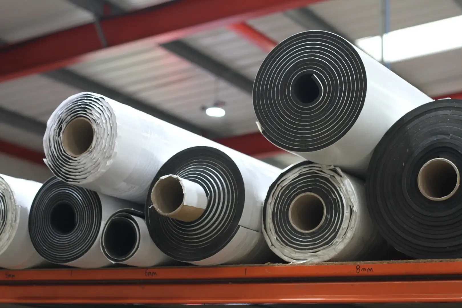 Rolls of rubber mattings stored stacked neatly under a warehouse roof