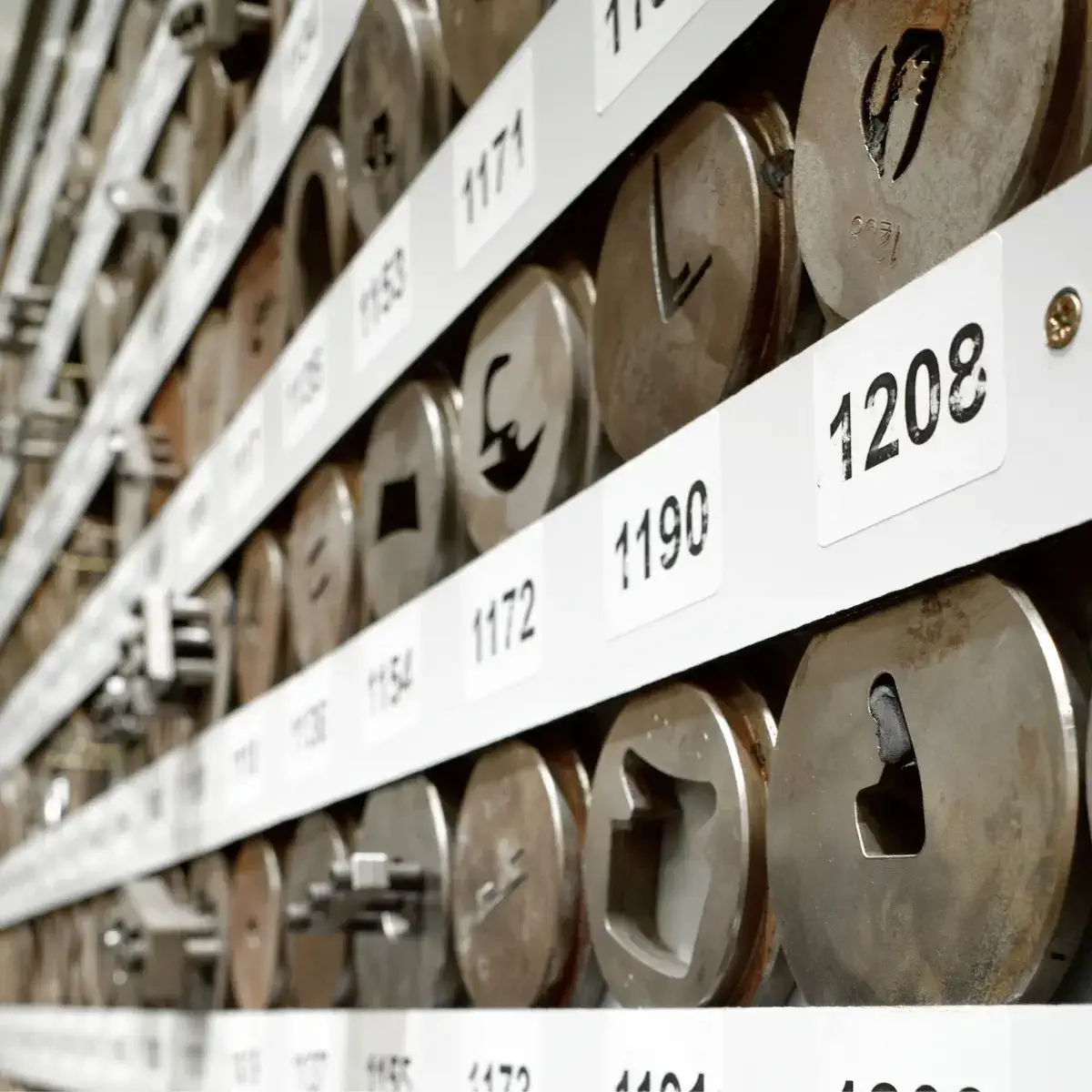 A large collection of metal dies with different shaped holes in each, stacked neatly on numbered shelves