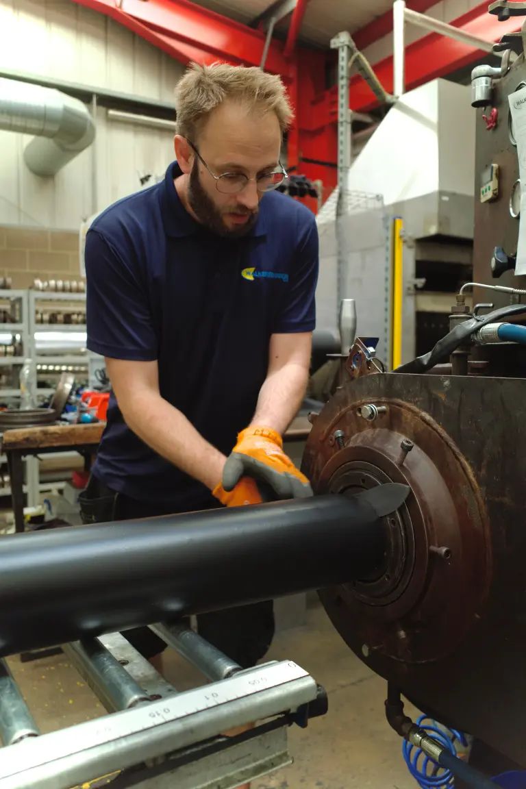 Manufacturing technician stands in busy factory setting while guiding rubber extrusion onto metal roller rack